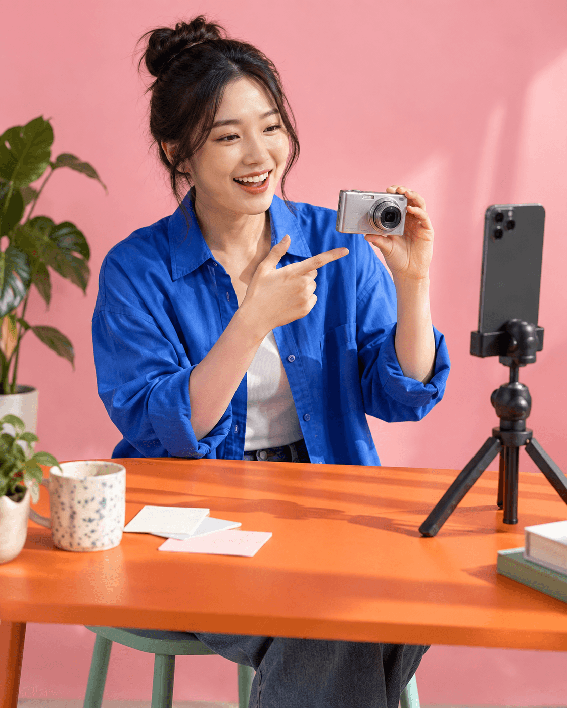 Original AI-generated concept photograph of a creator demonstrating a compact camera in a pink and cobalt studio